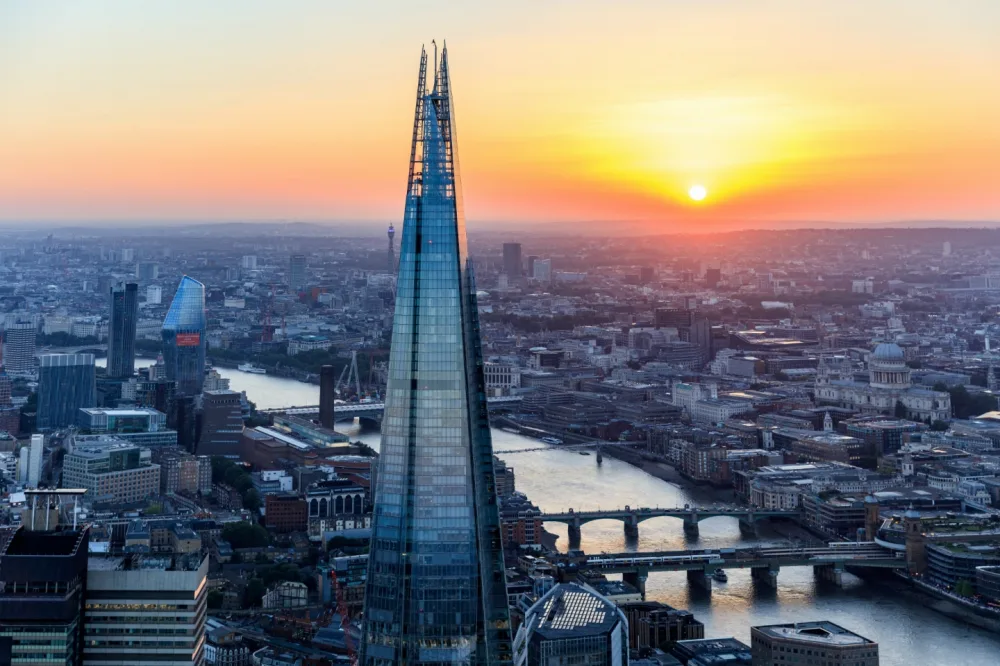 An aerial view of the River Thames with the Shard in the front and the sun setting in the background. 