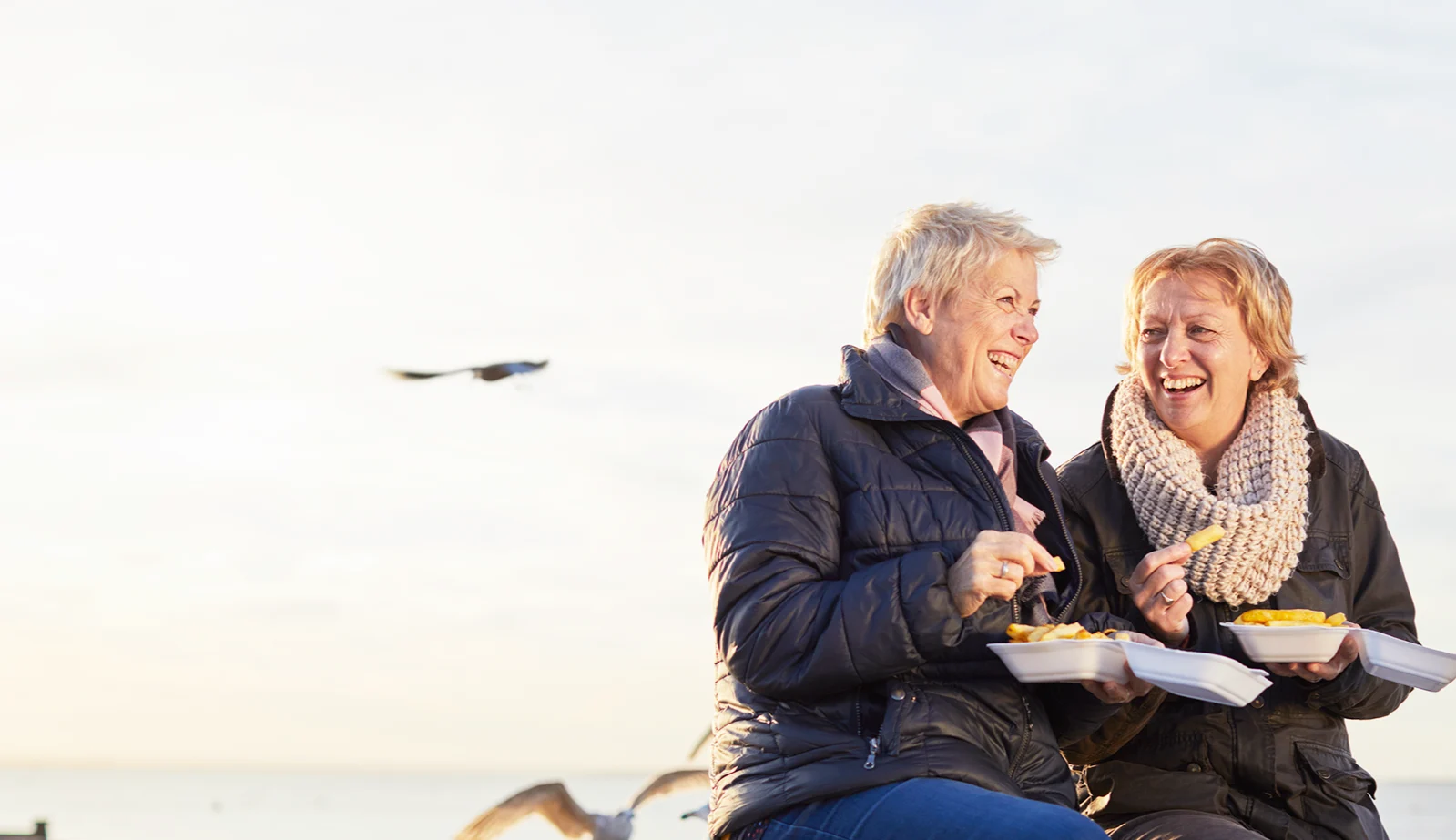 A middle aged lesbian couple eating fish and chips at the beach