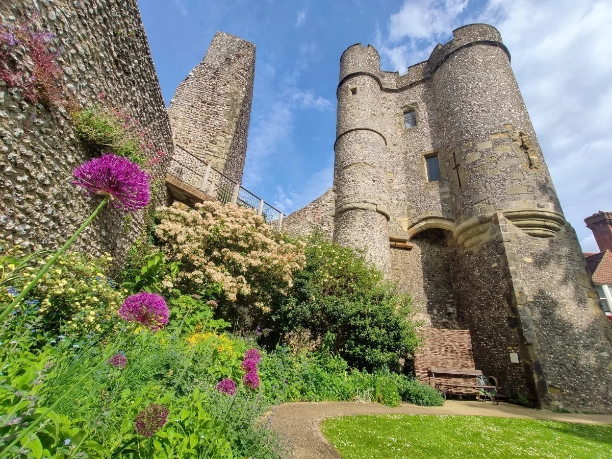 Looking up at a Norman castle made of stone, with blue sky above and grass and flowers in front. 