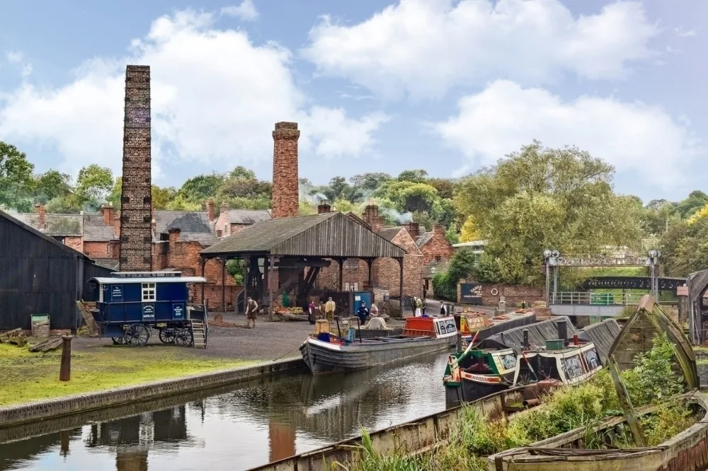 Old buildings and an outdoor awning sit on a canal with barge boats underneath a blue sky mixed with clouds.