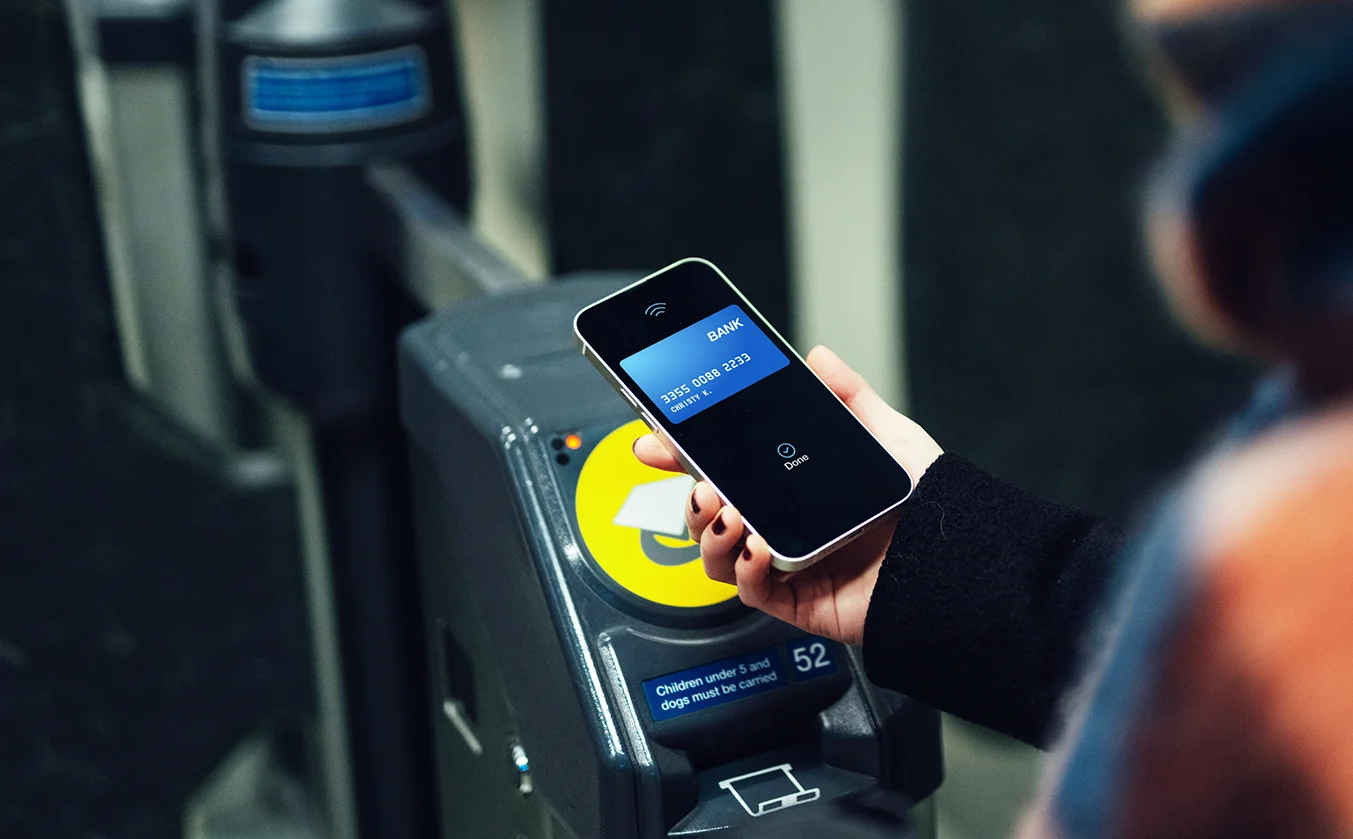 A woman uses contactless payment on her mobile phone to touch on a ticket barrier at a station