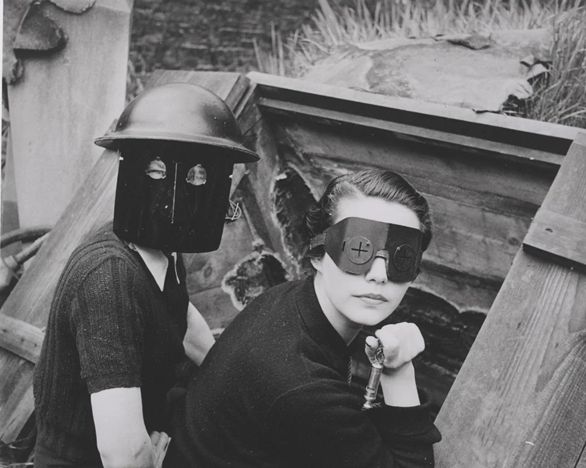 Black and white vintage photograph of 2 white women wearing unusual helmets and masks in a derelict building. 