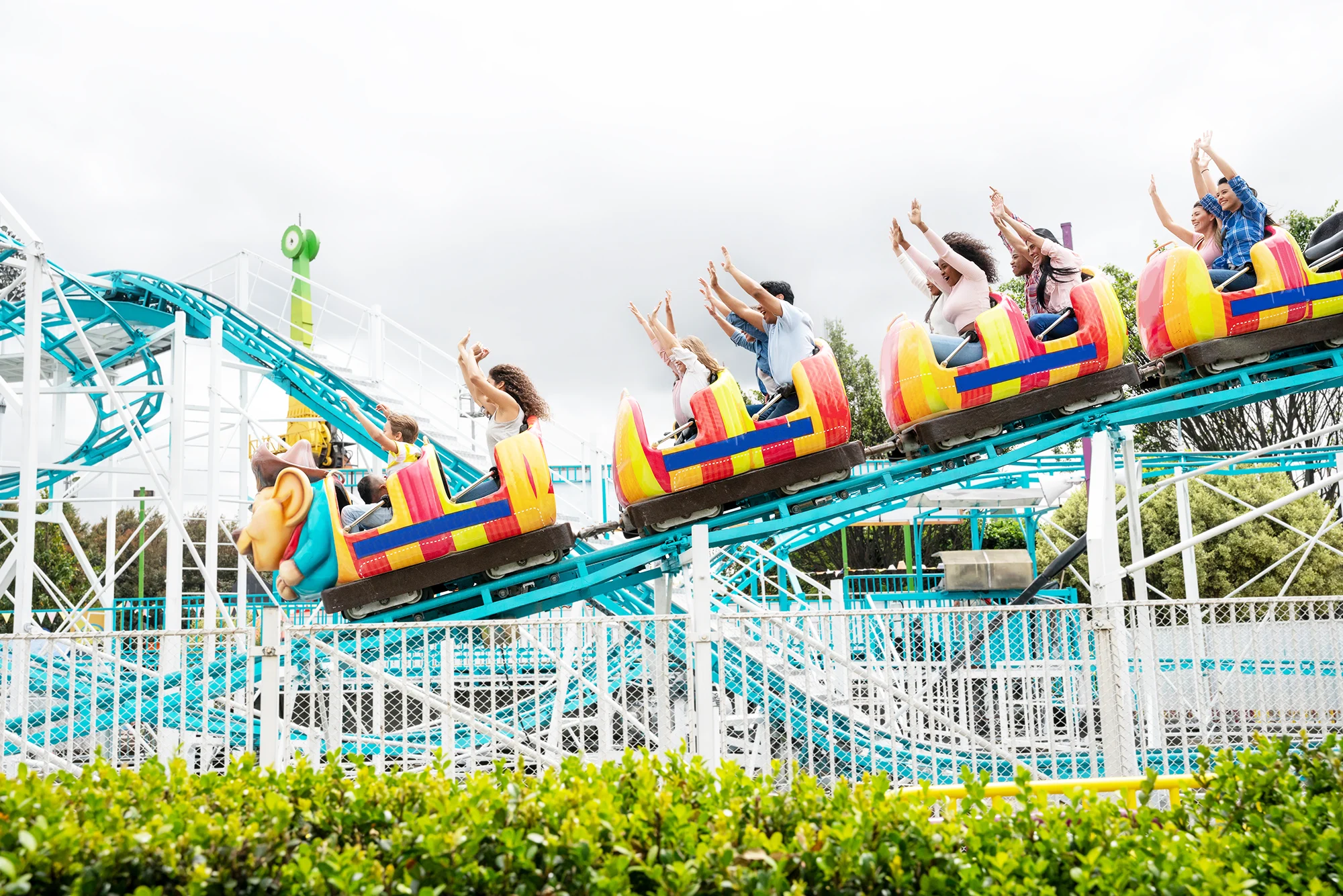 A side view of a group of people riding a roller coaster with their arms in the air