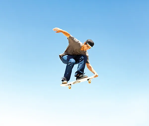 A young white man wearing a baseball cap and doing a jump trick on a skateboard.
