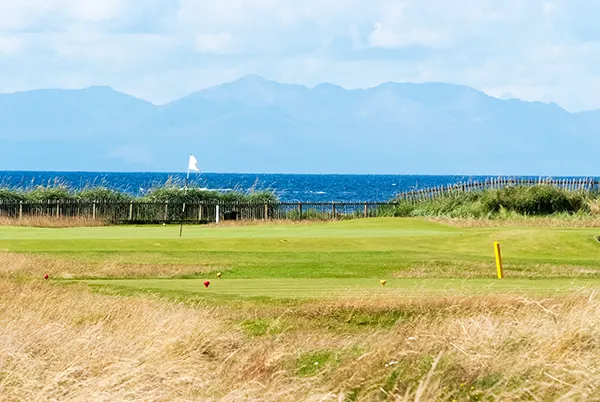A golf course next to the sea, with rugged mountains across the water.