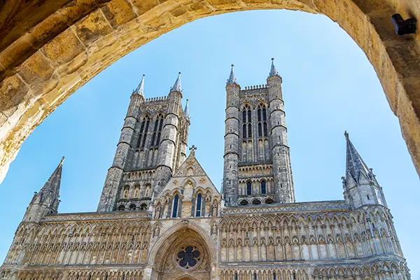 Looking up at a huge stone cathedral against a bright blue sky, with the view framed by a stone archway. 
