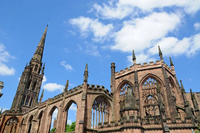 Image shows turret and top of coventry cathedral sitting beneath blue and cloudy sky.