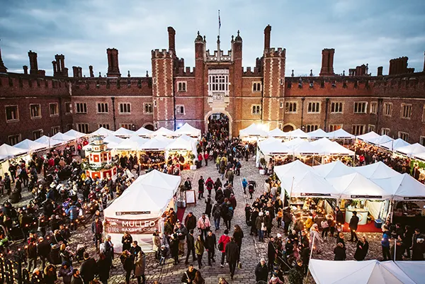 A large red brick palace with a courtyard full of people enjoying a Christmas market with food stalls.