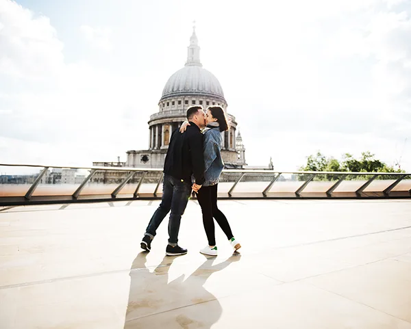 A young white man and white woman kissing on a bridge in front of St Paul's Cathedral.