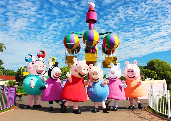 Peppa Pig character mascots standing in front of a fun fair ride. 