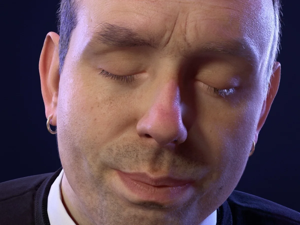 Close up image of white man with stubble and a hoop earring, he has his eye closed and looks peaceful. 
