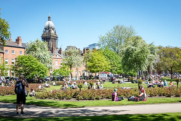 A city-centre park on a summer day with people sitting on the grass. 