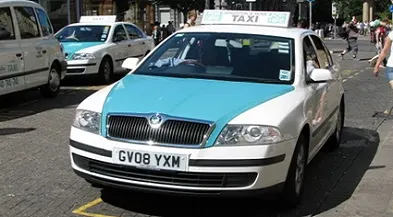 A light blue and white saloon car taxi at a taxi rank