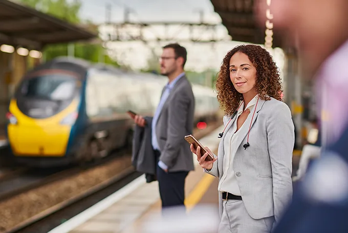 Business travellers standing on a railway platform holding mobile phones, a train is pulling into the opposite platform.