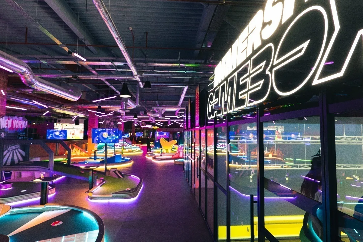 Modern gaming arcade with neon lights, illuminated mini-golf courses and bright signage in vibrant purple and blue.