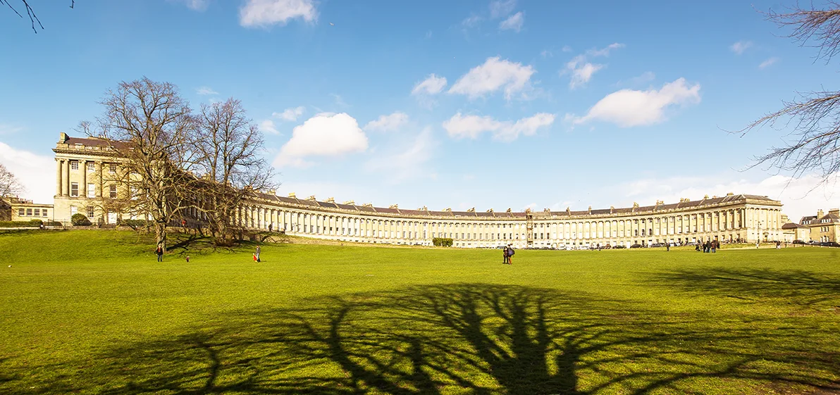 A green lawn with a sweeping crescent of Georgian townhouses behind, with a blue sky dotted with white clouds above.