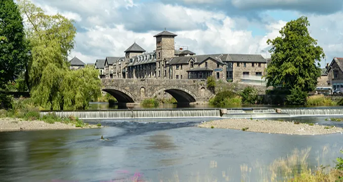 A large river with a stone bridge and large grey stone buildings in the background.