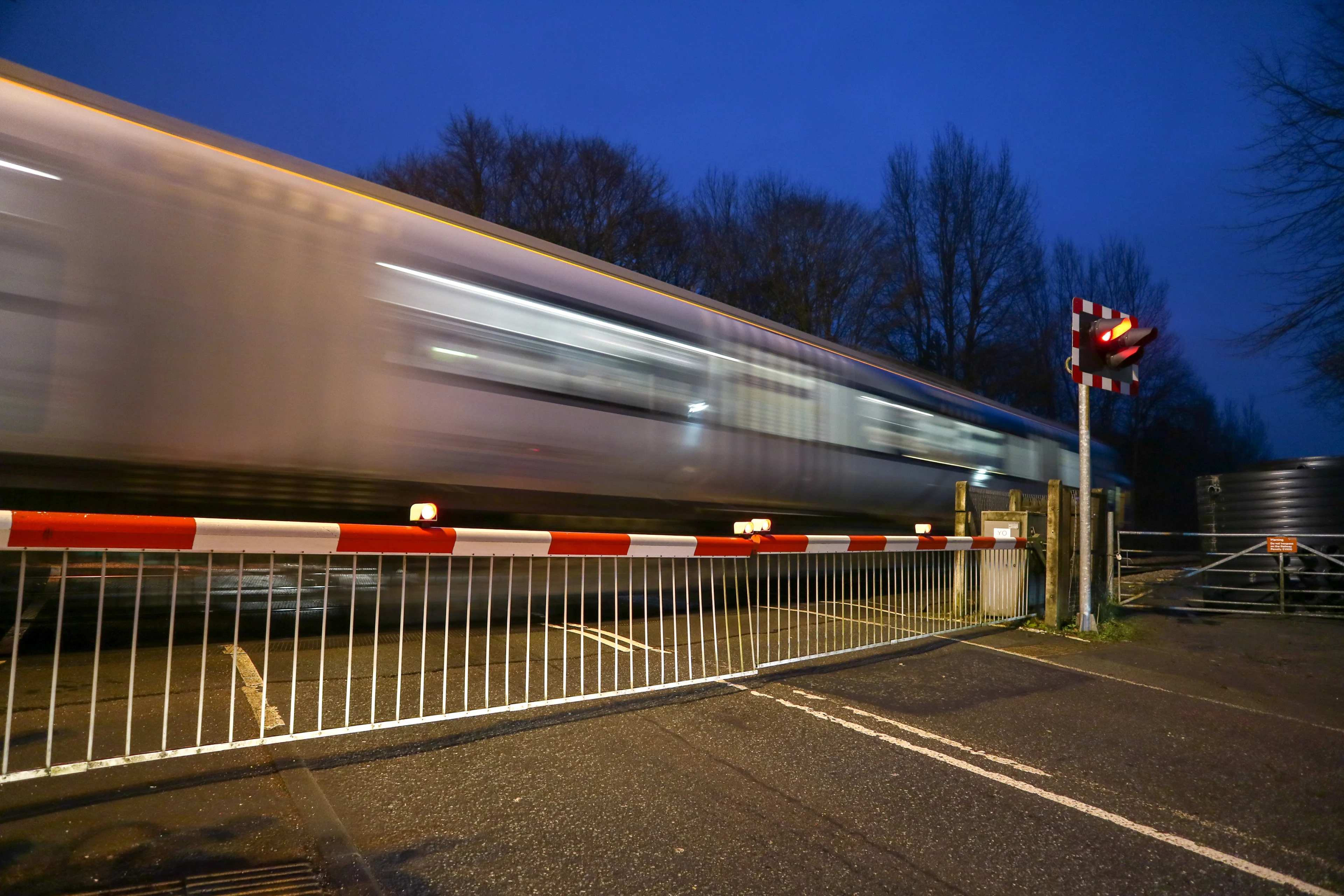 A train travelling at high speed past a level crossing with the barrier down and a red light signal