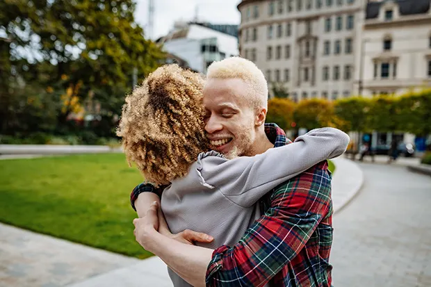 A Black man with albinism embracing a Black woman with a blonde twist hairstyle.