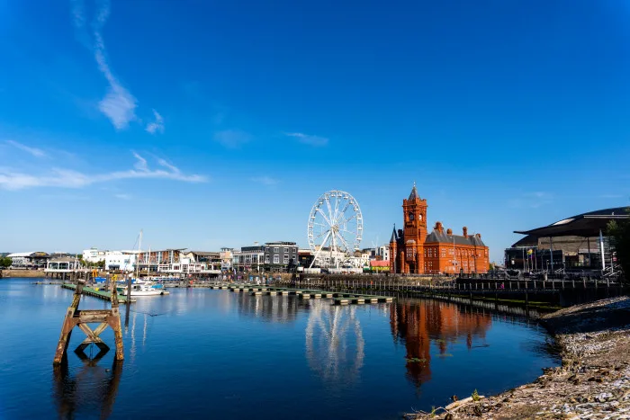 Buildings and ferris wheel overlooking the river Taff in the centre of cardiff with blue skies in the sunshine