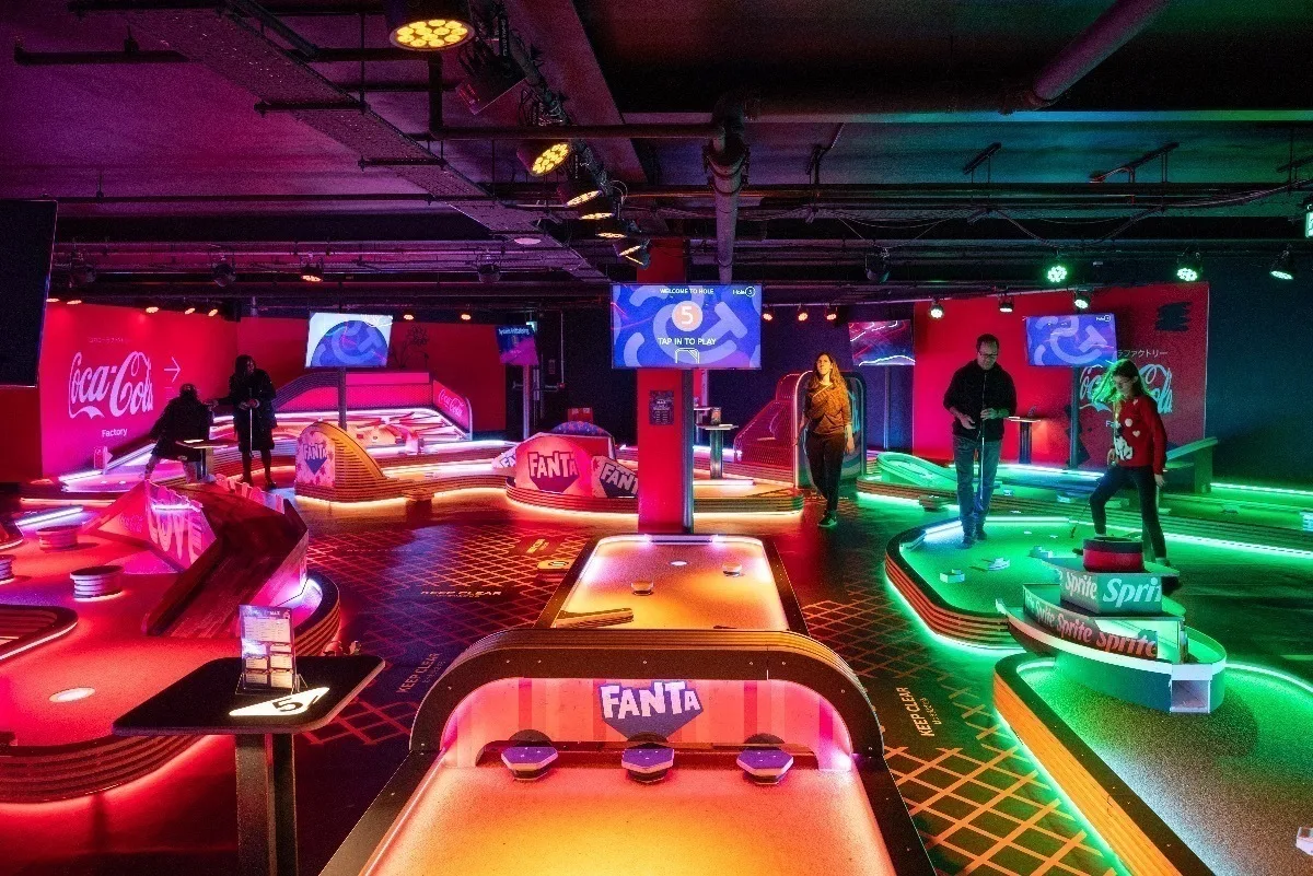 Vibrant indoor mini-golf course with neon lighting and players enjoying the game.