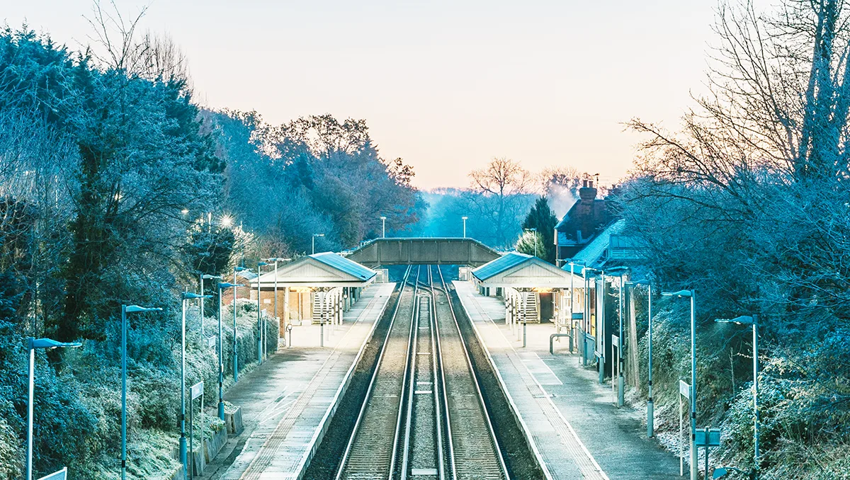 Early morning on a winters day, looking down the tracks at a rural train station with a bridge between the 2 platforms.