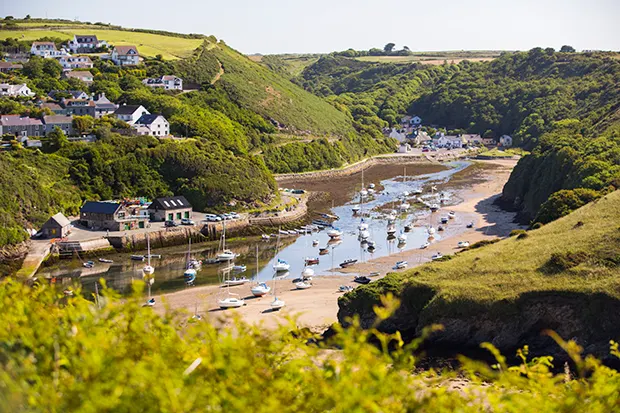 A sandy bay set among green hills, with a small village on the hillside and the water's edge. 