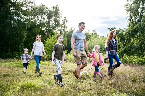 A white family (a man, a woman and 4 children) walking through a woodland area on a sunny day.