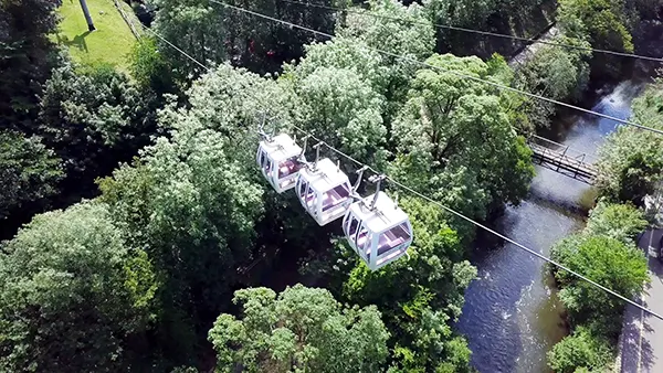 3 white cable cars suspended over a river and tall trees