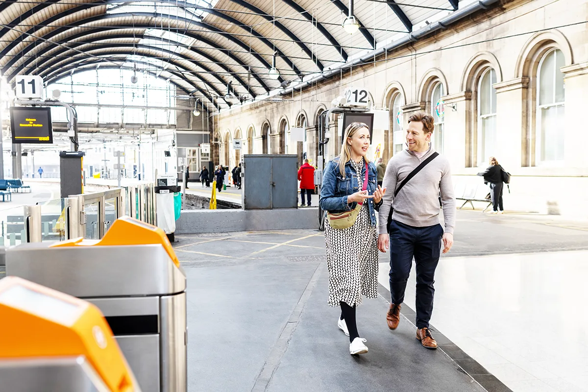 Two people walking through a train station with arched ceiling.