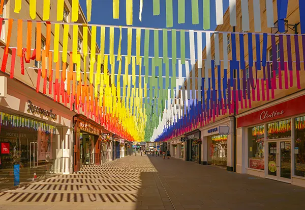 An empty pedestrian shopping street with rainbow bunting strung from side to side across the entire street.
