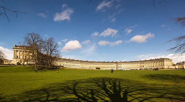 A green lawn with a sweeping crescent of Georgian townhouses behind, with a blue sky dotted with white clouds above.