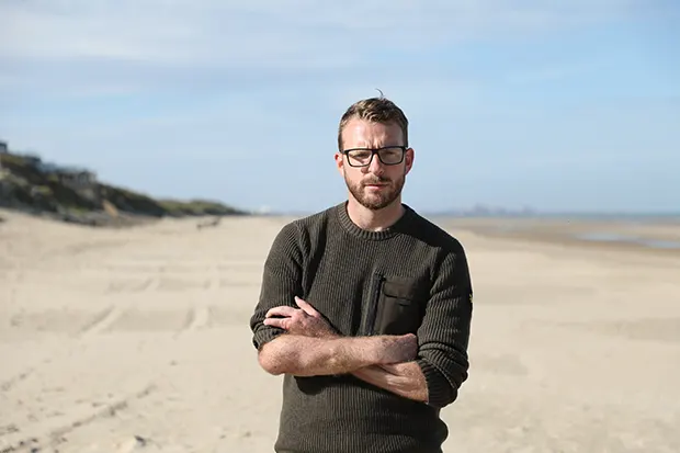 JJ Chalmers in a military sweater standing on a beach