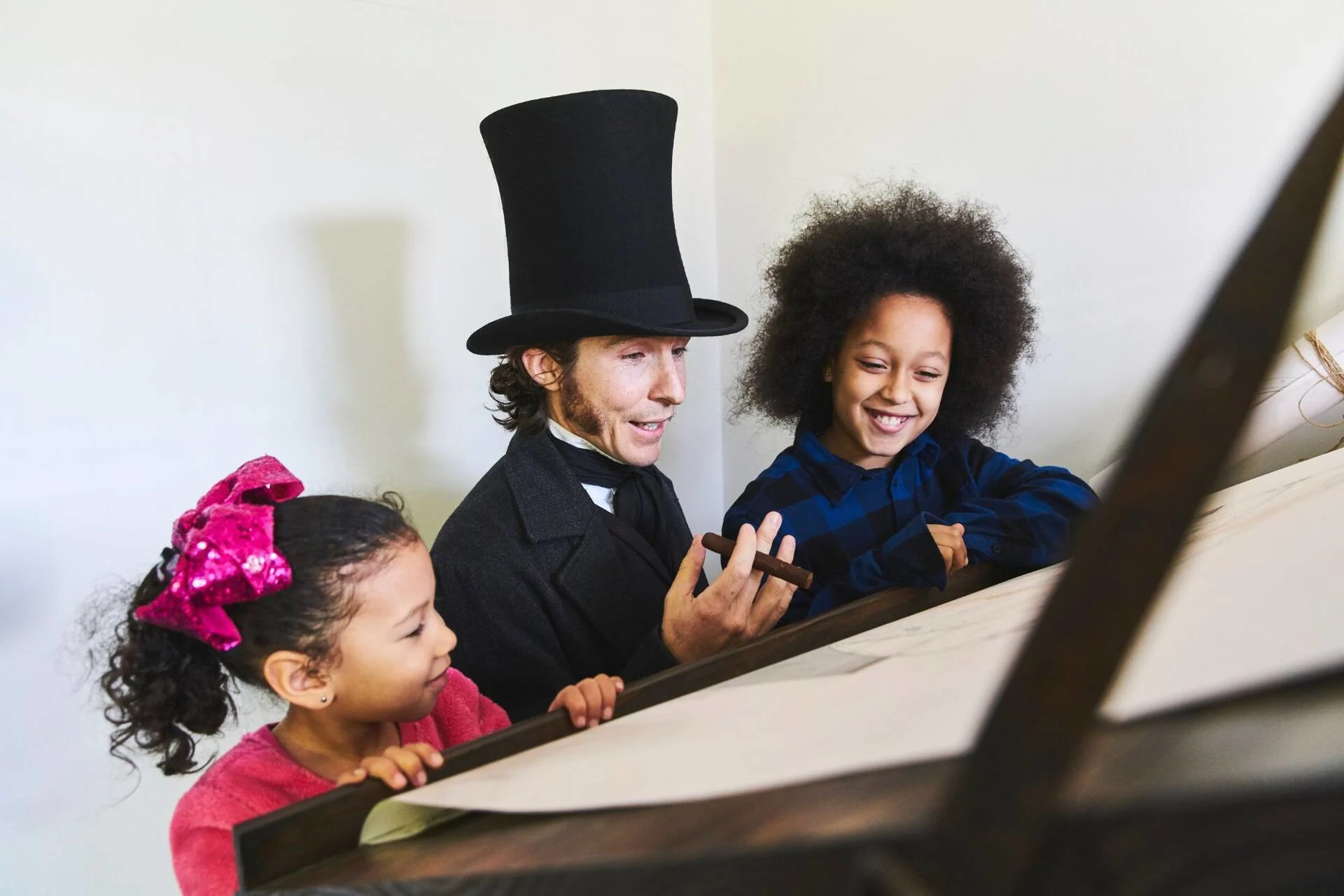 A white man in old-fashioned Victorian clothes looking at a display with 2 young Black girls.