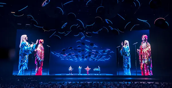 The stage of a performance of musical show ABBA Voyage, with holographic images of the band members on stage and huge screens showing them either side. 