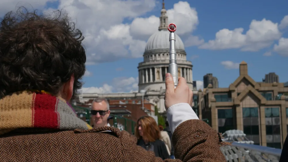 Back view of a man dressed as Dr Who holding a sonic screwdriver prop and facing St Paul's Cathedral from a bridge.