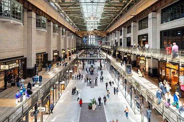 The interior of a large shopping centre with wide walkways and multiple levels. People are walking through the centre and there is a high glass roof above. 