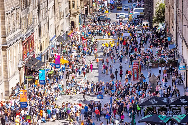 Crowds of people milling in a city street full of tents and performers on a sunny day. 