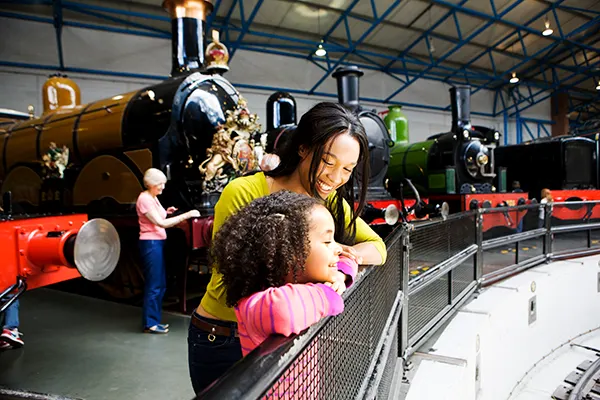 A Black woman and a Black girl enjoying a railway museum with vintage steam locomotives on display. 