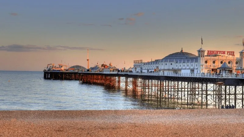 Brighton Pier at sunset over calm waters, with the pebble beach in the foreground.