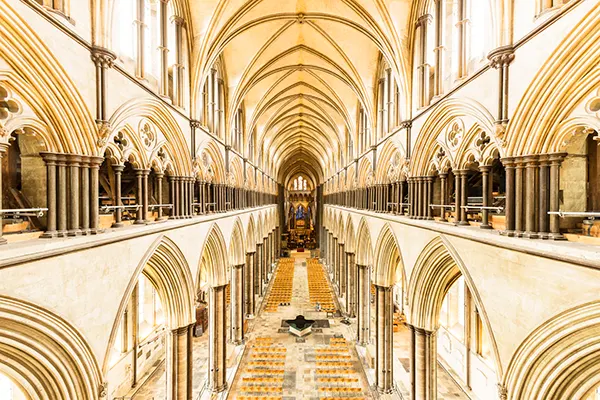 The inside of a large cathedral with stone arches and a high arched ceiling, looking down a narrow central aisle. 