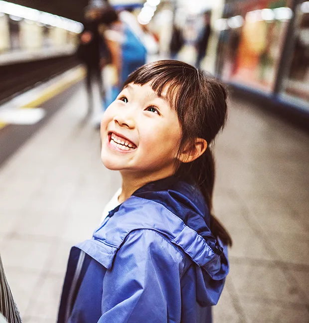 A young smiling East Asian girl on a train platform.